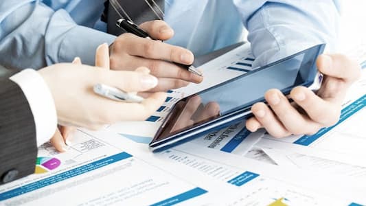 hands above papers next to digital screen 